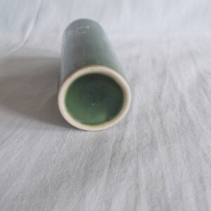 May include: A green ceramic vase with a white rim. The vase is cylindrical in shape and has a smooth, glossy finish.