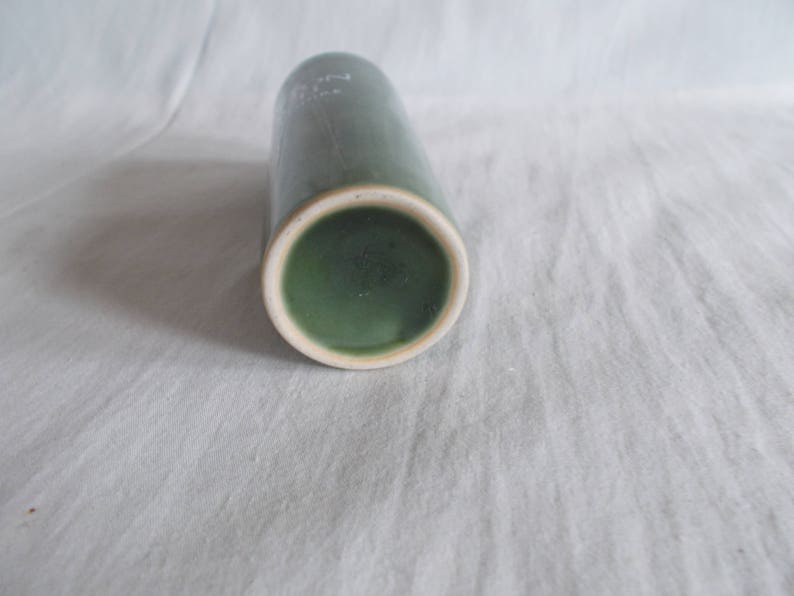 May include: A green ceramic vase with a white rim. The vase is cylindrical in shape and has a smooth, glossy finish.