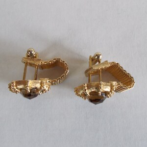 Pu&ograve; includere: Un paio di orecchini a clip dorati con una pietra marrone al centro. Gli orecchini hanno un design delicato e intricato.