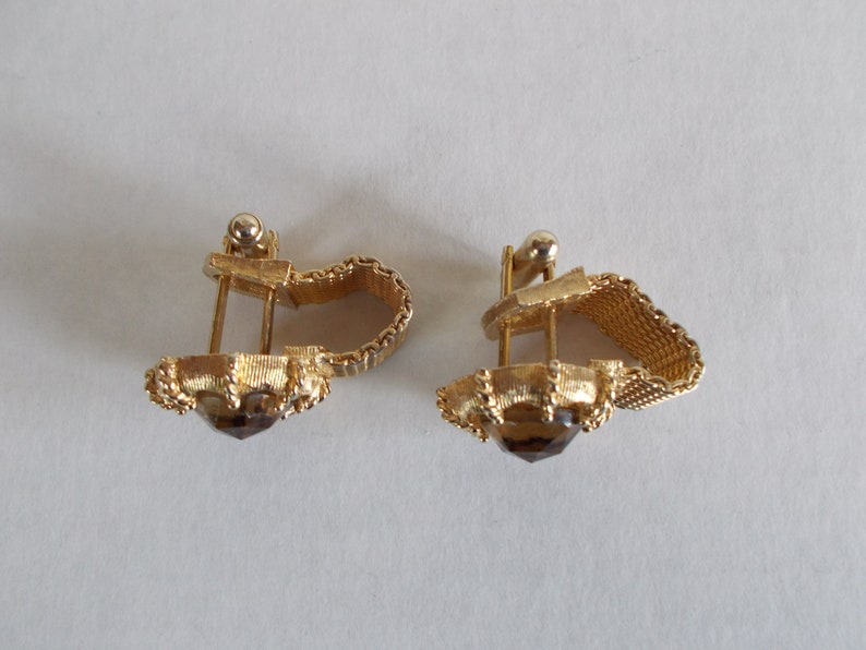 Pu&ograve; includere: Un paio di orecchini a clip dorati con una pietra marrone al centro. Gli orecchini hanno un design delicato e intricato.