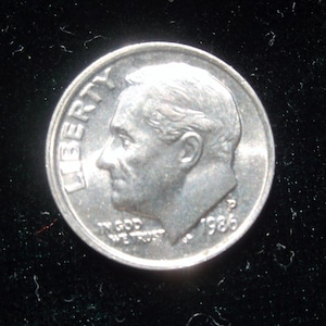 May include: A silver US dime coin with the year 1986 and the word "LIBERTY" inscribed on the side. The coin features a profile of Franklin D. Roosevelt.