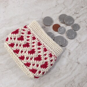 May include: A small crocheted coin purse with a red and white geometric pattern. The purse is open and filled with coins.