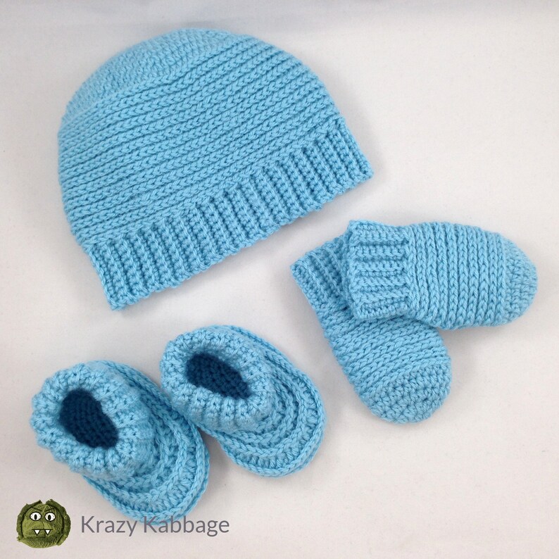 May include: A light blue, knitted baby set including a beanie hat, a pair of booties, and a pair of mittens. The set is made of a soft, textured yarn. The items are arranged on a white surface.
