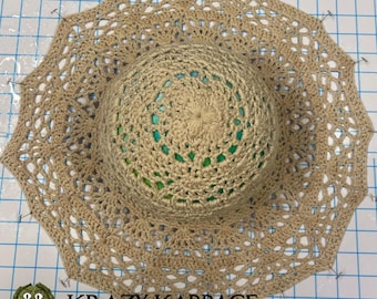 May include: A beige crochet hat with a lacy trim is pinned to a gridded surface. The hat is being prepared for sewing. The text "KRAZY KABBAGE" is visible at the bottom of the image.