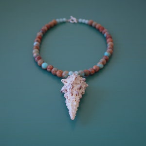 May include: A brown and blue beaded necklace with a white seashell pendant.