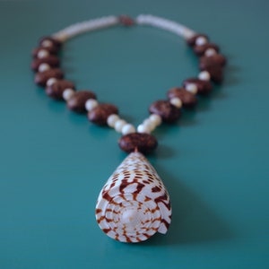 May include: A brown and white seashell necklace with a large, spiral seashell pendant. The necklace is made of brown and white beads and is strung on a white cord.