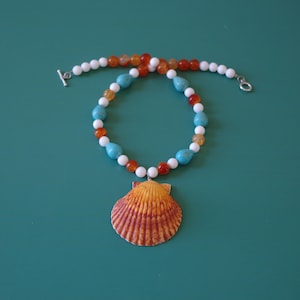 May include: A turquoise, white, and orange beaded necklace with a large seashell pendant. The seashell is orange and brown with a textured surface.