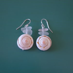 May include: A pair of silver earrings with white seashells and clear glass beads. The seashells have a spiral pattern with a pink center.