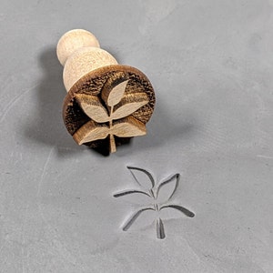 May include: A wooden stamp with a leaf design. The stamp is used to create an impression in clay or dough.