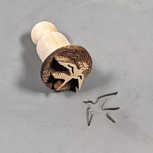 Peut inclure: Un tampon en bois avec un motif d'oiseau. Le tampon est utilisé pour créer des impressions dans l'argile ou la pâte.