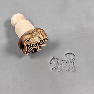 May include: A wooden stamp with a tiger design. The stamp is used to create an impression of a tiger in clay or dough.