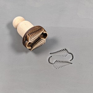 May include: A wooden stamp with a fern leaf design. The stamp is used to create an imprint of the fern leaf on clay or other materials.