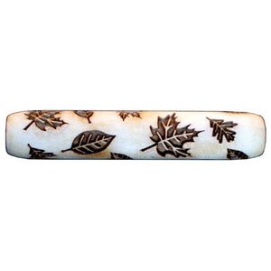 May include: A white wooden rolling pin with a brown leaf design. The leaves are in various sizes and shapes, and they are arranged in a random pattern.