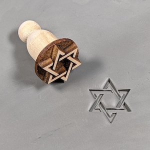 May include: A wooden stamp with a Star of David design. The stamp is used to create an impression in clay or dough.