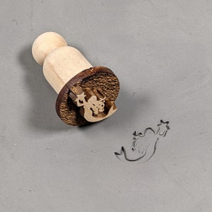 May include: Wooden stamp with a mermaid design. The stamp is mounted on a wooden handle. The mermaid is holding a star.