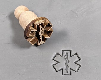 May include: A wooden stamp with a brown star of life design. The star of life is a symbol used by emergency medical services.