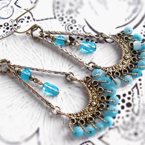 May include: A pair of silver dangle earrings with blue glass beads and a crescent moon design.