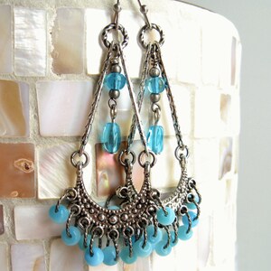 May include: Silver dangle earrings with a crescent moon design and blue glass beads.