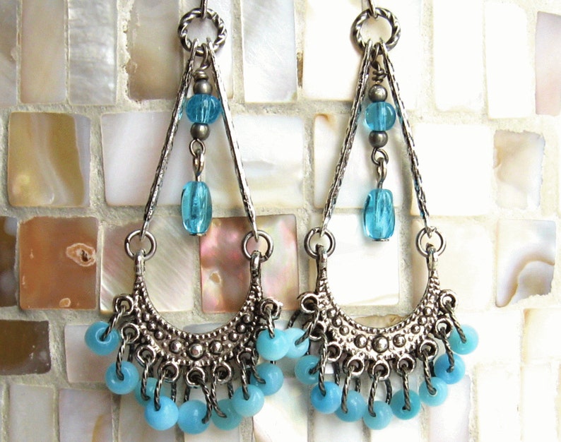 May include: Silver dangle earrings with a crescent moon design and blue glass beads. The earrings have a layered look with multiple strands of beads.