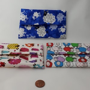 Peut inclure: Trois porte-mouchoirs en tissu avec des motifs de moutons. Le premier porte-mouchoir a un fond bleu avec des moutons blancs et des nuages. Le deuxième porte-mouchoir a un fond blanc avec des moutons colorés et des fleurs. Le troisième porte-mouchoir a un fond blanc avec des moutons colorés.