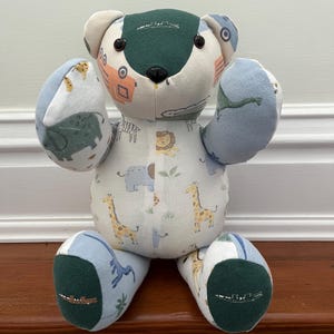 May include: A patchwork teddy bear with a safari animal print on a white body, blue and green accents, and black button eyes. The bear is handmade and sits on a wooden surface. The bear's height is approximately 30 cm.