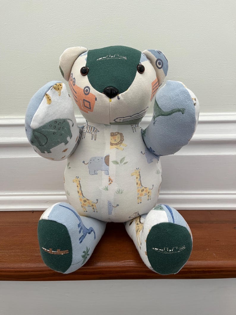 May include: A patchwork teddy bear with a safari animal print on a white body, blue and green accents, and black button eyes. The bear is handmade and sits on a wooden surface. The bear's height is approximately 30 cm.