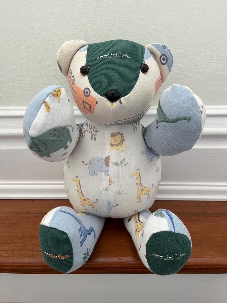 May include: A patchwork teddy bear with a green head and feet. The arms and legs are blue and white animal print fabric. The body is white with a repeating pattern of giraffes, lions, and elephants. The bear is handmade.