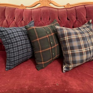May include: Three plaid cushions in shades of blue, green, and brown rest on a red velvet sofa. The cushions appear to be made from repurposed button-down shirts. The sofa has a carved wooden back.
