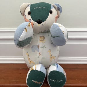 May include: A handmade patchwork bear toy. The bear has a green and cream-coloured head with black button eyes and a black nose. The body is white fabric printed with giraffes, elephants, and lions. The arms and legs are blue and green.