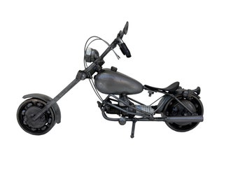 May include: A gray metal motorcycle model with a long, straight handlebar and a single seat. The motorcycle has a detailed design with visible engine parts and a gas tank.