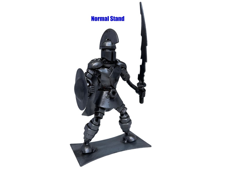 May include: A metal sculpture of a warrior holding a sword and shield. The warrior is made of recycled metal parts and is standing on a metal base. The sculpture is painted in a metallic gray color.