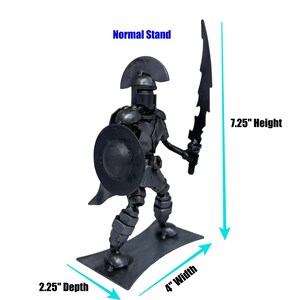 May include: A metal sculpture of a warrior holding a sword and shield. The sculpture is 7.25 inches tall, 4 inches wide, and 2.25 inches deep. The warrior is made of recycled metal and has a dark gray finish.