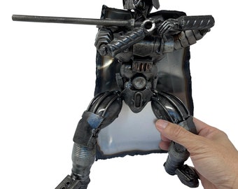 May include: A metal sculpture of Darth Vader from Star Wars, holding a lightsaber in a defensive stance. The sculpture is made of recycled metal parts and is painted black.