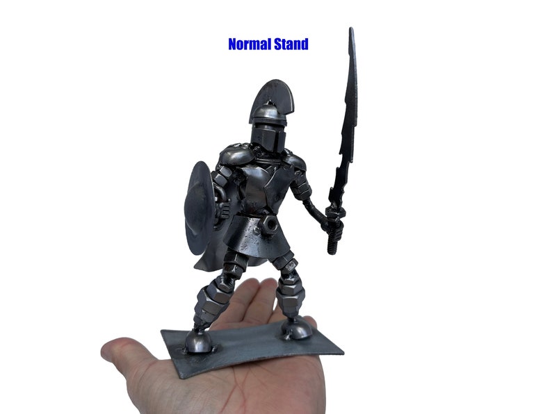 May include: A metal sculpture of a warrior holding a sword and shield. The warrior is standing on a metal base. "Normal Stand" is written in blue text above the sculpture.