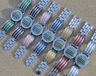 May include: Eight silver bracelets with different colored enamel inlays. The bracelets have a repeating link pattern and a round face with a grid design.
