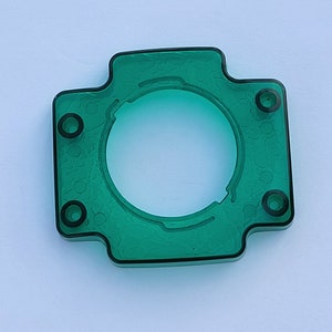 May include: A green plastic ring with four holes and a large center opening. The ring is designed to be used as a decorative element or a functional part.