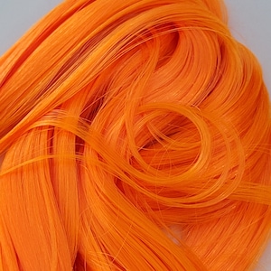 May include: A close-up of bright orange synthetic hair. The hair is long and straight, with a smooth texture.