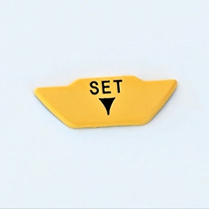 May include: Yellow plastic button with the word "SET" and a black triangle pointing down.