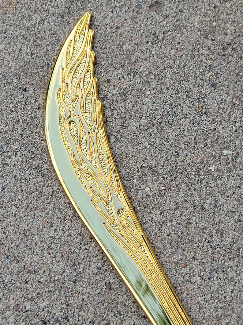 May include: A gold-colored, decorative knife with a curved blade and an intricate, floral design.