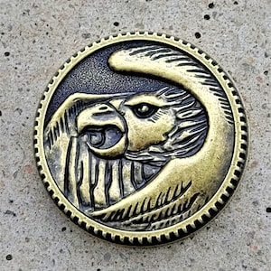 May include: A gold-toned metal pin with a detailed design of an eagle's head and wing. The eagle's eye is black and the pin has a textured surface.