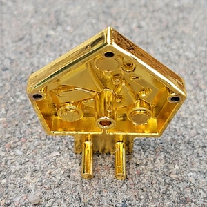 May include: Gold-colored metal object with a geometric shape and intricate details. The object has a hollow interior and appears to be a decorative piece.