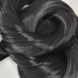 May include: A close-up of a bundle of long, black hair extensions. The hair is smooth and shiny, with a slight wave.