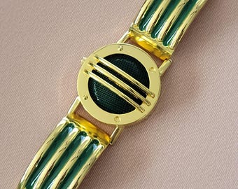 Könnte beinhalten: Goldfarbenes Armband mit grünem Emailleband und einem runden, goldfarbenen Zifferblatt mit grünem Zentrum.