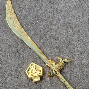 May include: A gold-colored sword with a decorative handle and a sheath with a Chinese character on it.