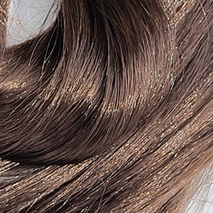 May include: Close-up of a bundle of brown hair extensions with a subtle shimmer.