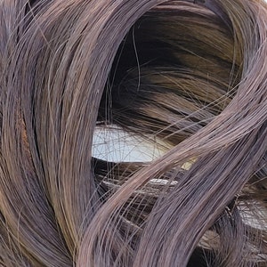 May include: A close-up of a bundle of dark brown human hair extensions.