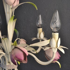 Pu&ograve; includere: Lampadario in metallo bianco con accenti di fiori rosa e bianchi e lampadine in vetro trasparente. Il lampadario ha un design floreale con foglie e fiori.