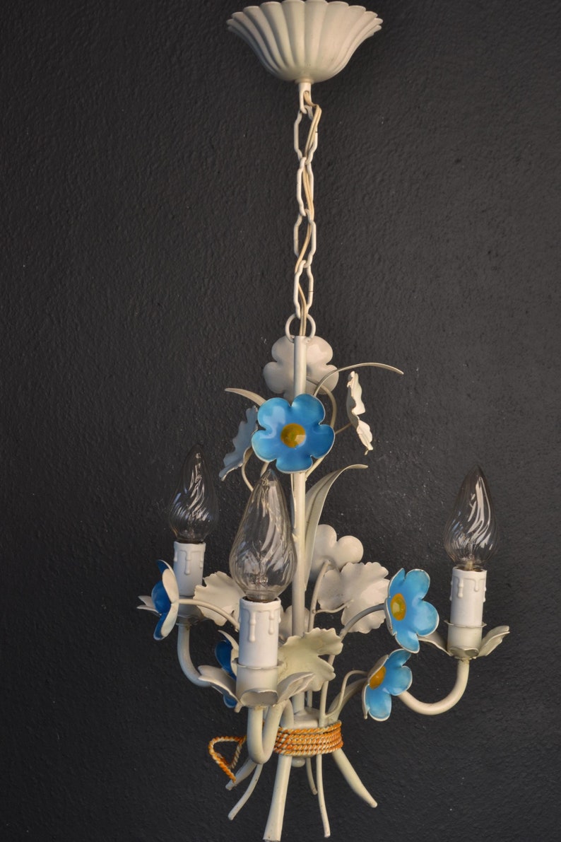 May include: White metal chandelier with blue and yellow flower accents. The chandelier has a white ceiling canopy and a chain.