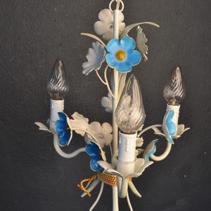 May include: White metal chandelier with blue flower accents and three clear glass bulbs. The chandelier has a floral design with delicate details.