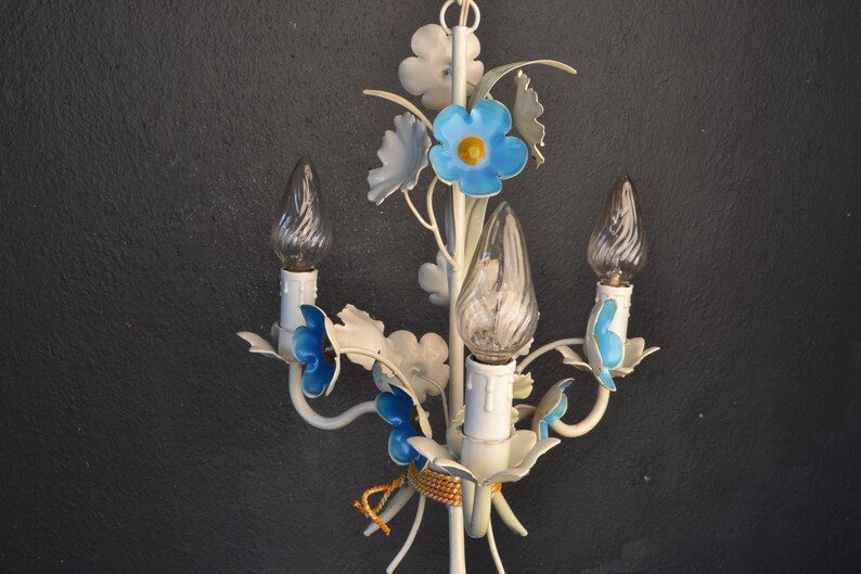 May include: White metal chandelier with blue flower accents and three clear glass bulbs. The chandelier has a floral design with delicate details.